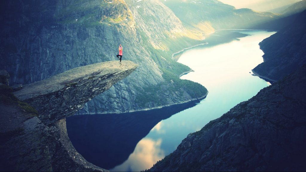 woman in yoga pose on rock above lake